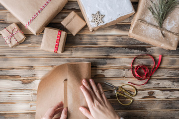 Woman packing handmade gifts made from kraft paper, christmas rope,  fir branches on the rustic wood planks background. DIY. Flat lay.