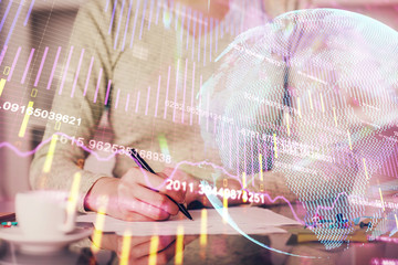 Hand taking notes in notepad. Forex chart holograms in front. Concept of research. Double exposure