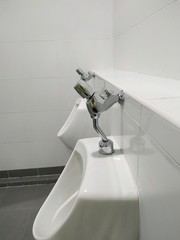 Silver faucets of white urinal in the toilet room.
