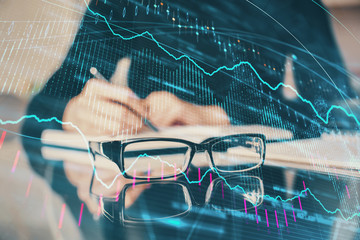 Forex chart hologram on hand taking notes background. Concept of analysis. Multi exposure