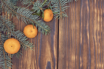 Tangerines and fir branches on a rough wooden background.