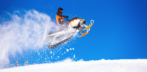 snowmobile jump straight up. the guy is flying and jumping on a snowmobile on a background of blue sky leaving a trail of splashes of white snow. bright snowmobile and suit. No brands. copy text - obrazy, fototapety, plakaty