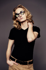 Obraz premium Young handsome guy with long blonde hair in a black T-shirt on a gray background with glasses kaleidoscopes.