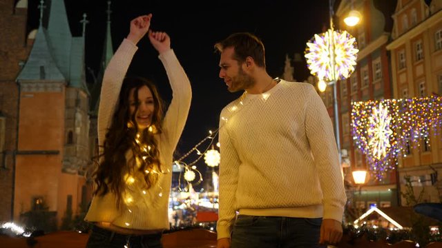 Young cute couple people have fun dancing on christmas fair market bright illuminated market square in city center