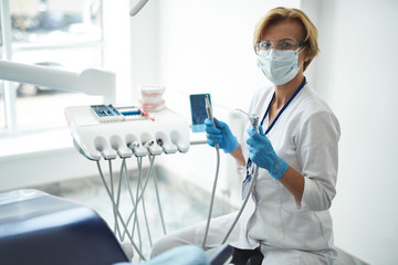 Pleasant female dentist using her equipment at work