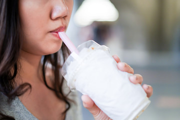 Asian woman drinking iced coffee by using a plastic straw close up.