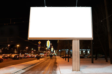 advertising billboard in the city at night in winter. Ad design mockup with white field. near the road