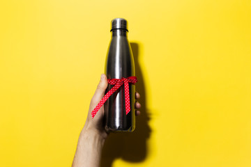 Close-up of male hand holding a eco water thermo bottle of steel with red ribbon, ecologic gift for...