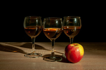 Three glasses with calvados and an apple stand on a table against black background