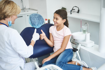 Cheerful dentist and teenage lady are displaying appreciating hand gesture