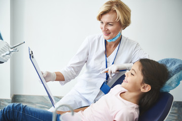 Optimistic dentist is showing diagnosis on clipboard to young patient
