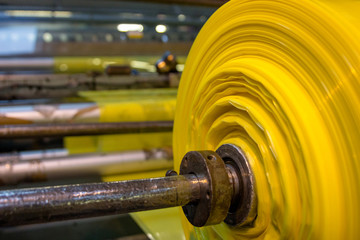 Imagery of Yellow spool plastic packaging sheet heavy duty for industrial use outdoors wrapped around a worn metal pole ready to feed into machine for cutting into shape or printing logos or branding
