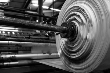 B&W imagery of spool of plastic packaging sheet heavy duty for industrial use outdoors. wrapped around a metal pole ready to feed into a machine for cutting into shape or printing logos or branding