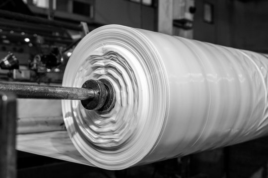 B&W imagery of spool of plastic packaging sheet heavy duty for industrial use outdoors. wrapped around a metal pole ready to feed into a machine for cutting into shape or printing logos or branding
