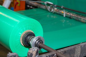 Imagery of green spool of plastic packaging sheet heavy duty for industrial use outdoors. wrapped around a worn metal pole ready to feed into a machine for cutting into shape or printing logos.