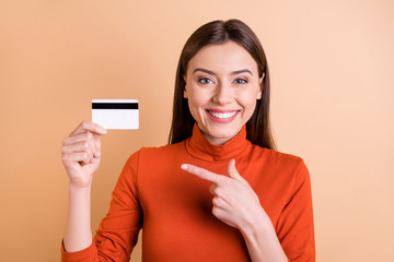 Photo of charming cute cheerful girlfriend showing you that using electronic way of payment is more comfortable holding credit card with her hand pointing isolated beige pastel color background