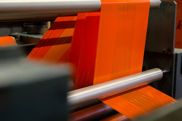 image of the inside workings of a machine with orange high vis plastic sheet being fed through...