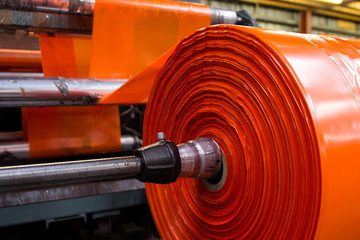 image of the inside workings of a machine with orange high vis plastic sheet wrapped around a metal shiny but dirty and greasy pole, in a spool to be fed into the industrial machine looking abstract 