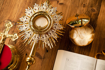 Catholic religion symbols. The Cross, monstrance,  Holy Bible and golden chalice on the rustic wooden table.