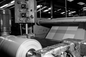 Black & White imagery of spool of plastic packaging sheet heavy duty for industrial use outdoors. wrapped around a metal pole ready to feed into a machine for cutting into shape or printing logos.