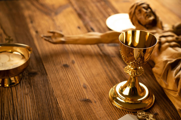 Catholic religion symbols.  Jesus figure and golden chalice on the rustic wooden table.