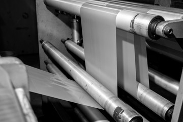 Black & White imagery of spool of plastic packaging sheet heavy duty for industrial use outdoors. wrapped around a metal pole ready to feed into a machine for cutting into shape or printing logos.