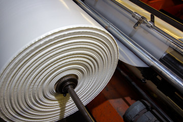 image of the inside workings of a machine with white high vis plastic sheet being fed through industrial factory on rollers with tension keeping it straight being stretched and cut ready for packing