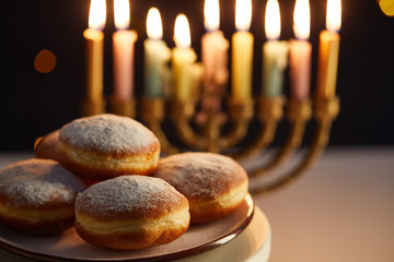 selective focus of delicious doughnuts on stand near glowing candles in menorah on black background...