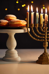 delicious doughnuts on stand near glowing candles in menorah on black background with bokeh lights...
