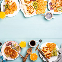 Food background with healthy breakfast with fresh hot waffles hearts, pancakes flowers with berry jam and fruits on turquoise table, top view, flat lay, copy space.