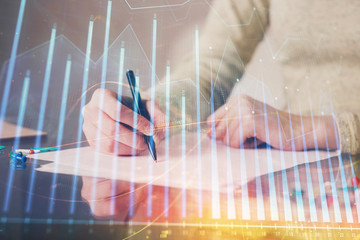 Hand taking notes in notepad. Forex chart holograms in front. Concept of research. Multi exposure