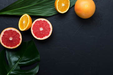 Top view of ripe and juicy oranges, grapefruit, green exotic leaves on the back surface.Empty space for design
