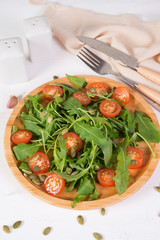 Fresh vegetable salad. Vegetarian salad of arugula, cherry tomatoes and pumpkin seeds in a wooden plate. The concept of pure and natural food.