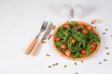 Fresh vegetable salad. Vegetarian salad of arugula, cherry tomatoes and pumpkin seeds in a wooden plate. The concept of pure and natural food. Horizontal photo with copy space