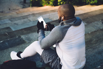 Athletic black man with smartphone sitting on steps