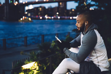 Sportive man thoughtfully looking at smartphone in embankment