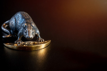 A metal rat figurine holds golden cheese. The concept of well-being and prosperity in 2020. On a black background. space for text. Silver and gold item. Christmas background.