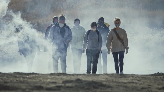 Group of young people in gas mask going through the toxic smoke in a desolate and burned out forest landscape.