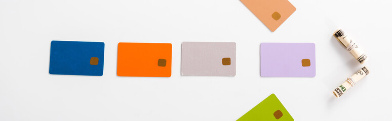 panoramic shot of colorful credit card templates and cash rolls on white