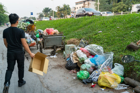 Pile of garbage bags and messy trash on street sidewalk with traffic on background in Hanoi, Vietnam. A man dumping rubbish into dustbin