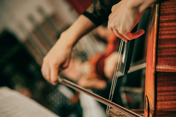 Symphony orchestra on stage, hands playing cello. Shallow depth of field, vintage style.