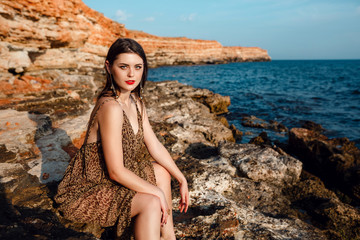 The young beautiful woman with tan on the beach, near the rocks