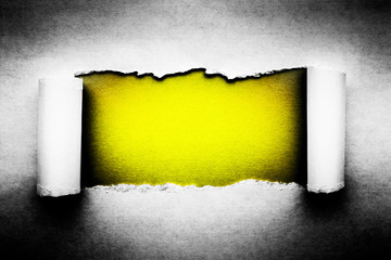 A hole in vintage paper with torn edges close-up with a yellow vibrant color background inside.