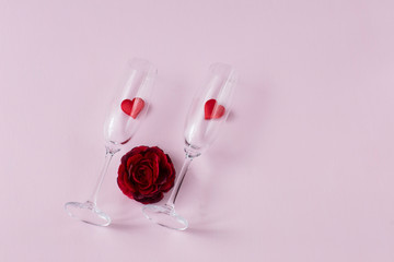 on a pink background, two glasses with hearts and a red rose bud