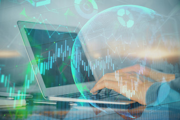 Double exposure of businessman's hands with laptop and stock market graph background. Concept of research and trading.