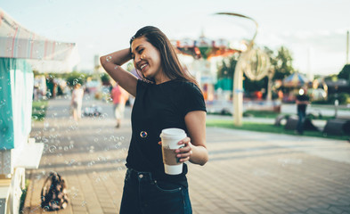 Happy asian young woman in casual wear holding coffee to go enjoying soap bubbles in air while recreating on vacation in city festival, cheerful hipster girl entertaining in park on weekends.