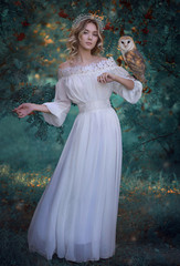 Art photo: growth photo of a fairytale girl with an owl in a barn owl in a long white dress