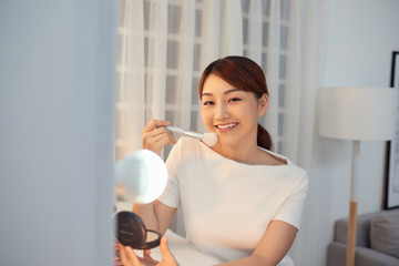 Happy young Asian woman applying makeup on face with big brush