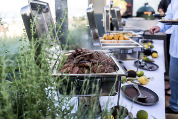 Grillbuffet mit Fleisch und Gemüse und Menschen im Hintergrund
