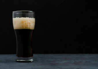 A pint of dark beer with foam, Dark background.